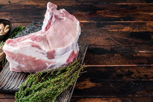 Raw rack of pork loin chops with ribs on a butcher board with meat cleaver. Dark wooden background. Top view. Copy space.