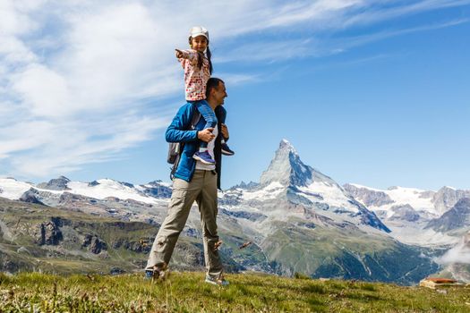 Happy family with little child doing trekking on switzerland mountain in summer time. Young people having fun in landscape nature. Concept of travel, friendly family.