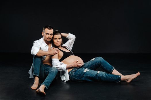 a pregnant woman and a man in a white shirt and jeans in a studio on a black background.