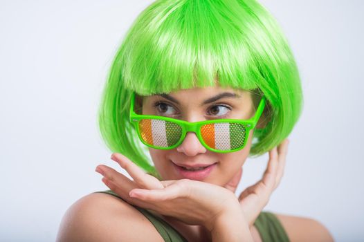 Cheerful young woman in green wig and funny glasses celebrating st patrick's day on a white background.