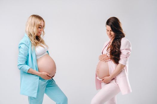 Two pregnant women with big bellies in suits on a gray background.