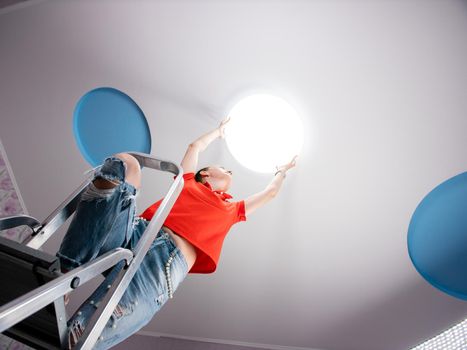 The girl hangs a ceiling lamp in the room.