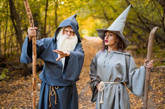 Wizard and sorceress in the autumn forest. Elderly man and woman in carnival costumes for halloween.