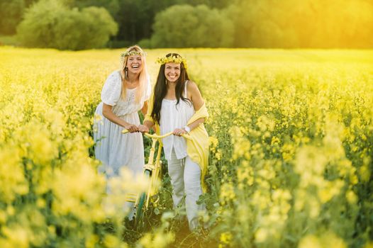 two women in a rapeseed field with a bicycle enjoy a walk in nature rejoicing.