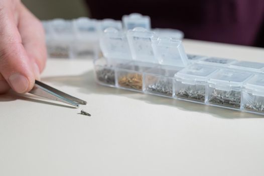 A close-up of male hands takes a screw for repairing glasses with tweezers.