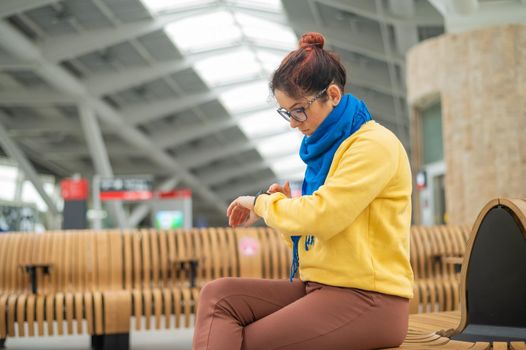 Caucasian woman sitting at the railway station and looking at smart watch