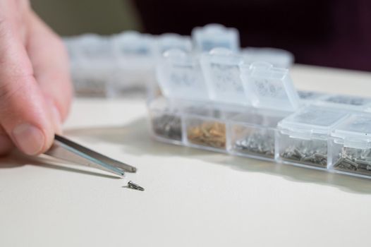 A close-up of male hands takes a screw for repairing glasses with tweezers.