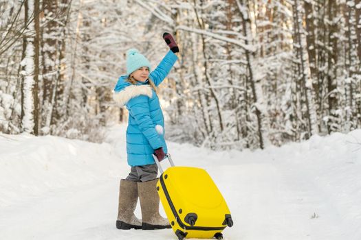 A girl in winter in felt boots goes with a suitcase on a frosty snowy day.