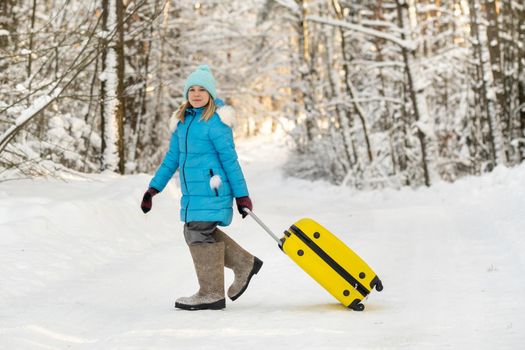 A girl in winter in felt boots goes with a suitcase on a frosty snowy day.