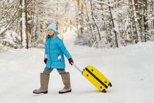 A girl in winter in felt boots goes with a suitcase on a frosty snowy day.