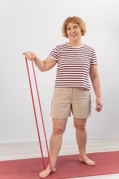 An elderly woman is engaged in fitness with an elastic band on a white background.