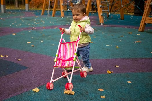 cute toddler kid carries a baby stroller for a walk in the autumn park.