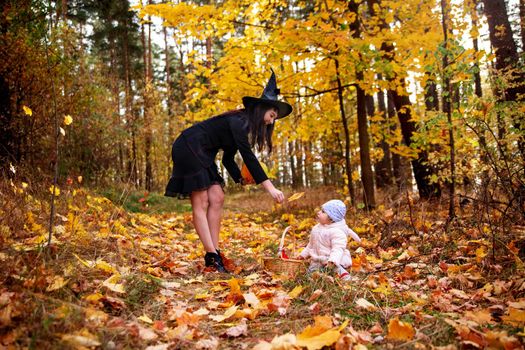woman witch plays with a small child in the autumn forest. halloween concept costumes. witch and bunny. concept of friends mother and daughter