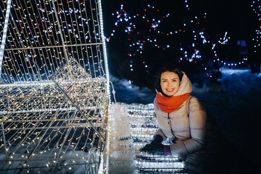 a girl in a gray jacket in winter with evening lights burning on Christmas street.