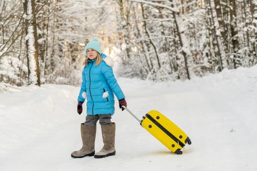 A girl in winter in felt boots goes with a suitcase on a frosty snowy day.