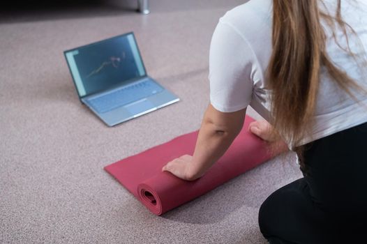 Young chubby woman folds sports mat after online fitness class.