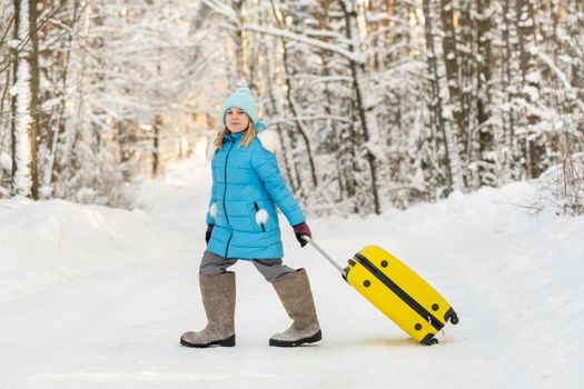 A girl in winter in felt boots goes with a suitcase on a frosty snowy day.