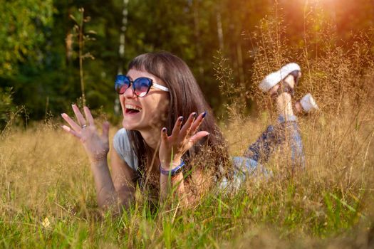 beautiful young woman in sunglasses enjoys the sun on the grass in warm sunshine