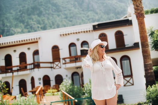 A beautiful girl in a tunic and hat stands near a Villa with a beautiful view.A woman enjoys a holiday in a Turkish resort.