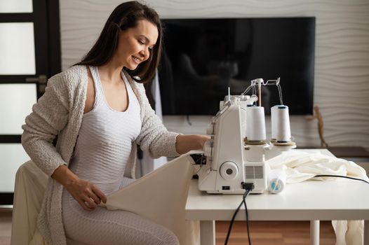 Caucasian woman sews to order at home. Work space of a seamstress in the living room.