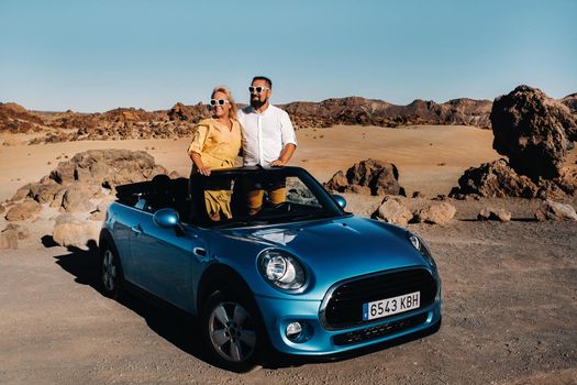 a woman and a man wearing glasses in a convertible car on a trip to the island of Tenerife. The crater of the Teide volcano, Canary Islands,Spain.