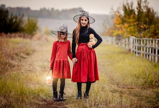 Girls with halloween decorations holding hands standing on autumn nature