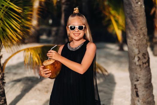Portrait of a cheerful 9-year-old girl with a coconut cocktail on the background of palm trees on an exotic beach.little Girl with a coconut on the beach of the island of Mauritius.