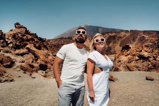 a guy and a girl in white clothes and glasses stand in the crater of the El Teide volcano, a Couple stands on a mountain in the crater of a volcano on the island of Tenerife, Spain