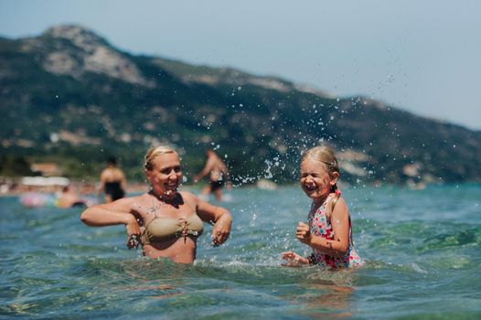 mother with daughter plays in the water, beautiful swimwear, laughs and smiles, splashes of water.