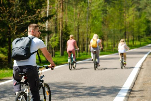 A group of cyclists with backpacks ride bicycles on a forest road enjoying nature.