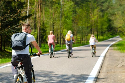 A group of cyclists with backpacks ride bicycles on a forest road enjoying nature.