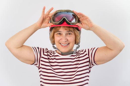 An elderly woman puts on a pink ski helmet on a white background.