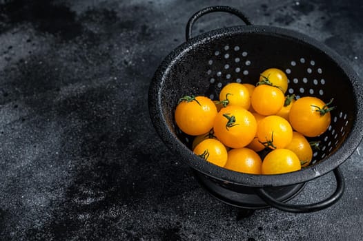 Yellow cherry tomato in a colander. Black background. Top view. Copy space.