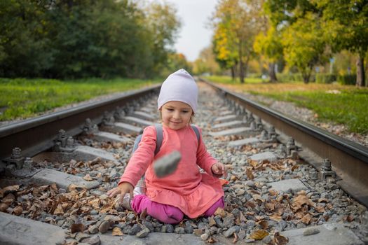 little girl sitting on the railroad tracks. toddler plays on railroad in forest