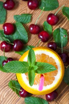 ripe orange with cut up top and red cherry on a wooden table, close-up, top view