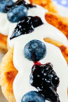 dessert, made from cottage curd cheese, poured thick cream with blueberry cream and whole bog whortleberry berries, close-up