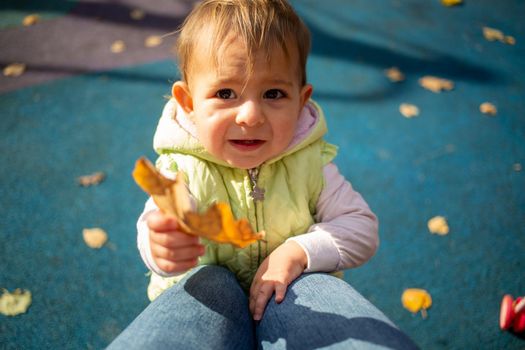 Cute one-year toddler girl with emotion holds out a yellow oak leaf to the camera. close-up. child portrait in autumn.
