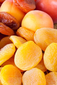 a pile of orange and yellow dried dried apricots, lying together with fresh and ripe apricots on a wooden table, close-up photo