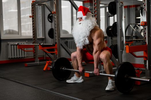 Santa claus in the gym. Muscular man with a naked torso doing exercises with dumbbells