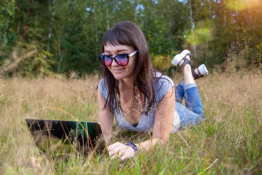beautiful young woman emotionally working on a laptop on a sunny lawn on a warm summer day. happy remote freelancer