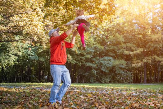 dad and child are playing in the park. dad tosses Toddler's daughter.