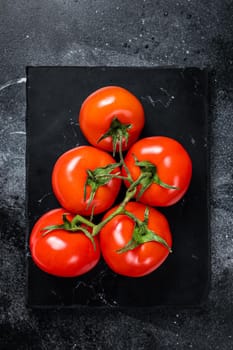 Branch of Red cherry tomatoes on marble board. Black background. Top view.