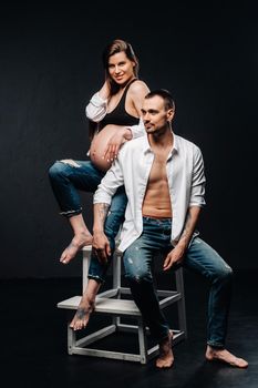 a pregnant woman and a man in a white shirt and jeans in a studio on a black background.