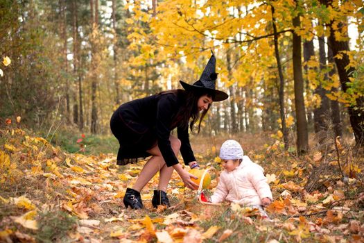 woman witch plays with a small child in the autumn forest. halloween concept costumes. witch and bunny. concept of friends mother and daughter