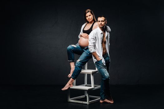 a pregnant woman and a man in a white shirt and jeans in a studio on a black background.