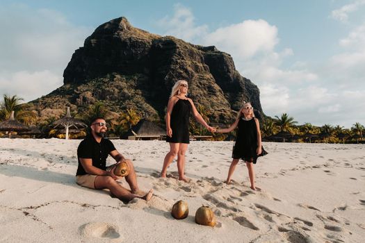 a stylish family in black clothes with coconuts in their hands on the beach of the island of Mauritius.Beautiful family on the island of Mauritius in the Indian ocean.