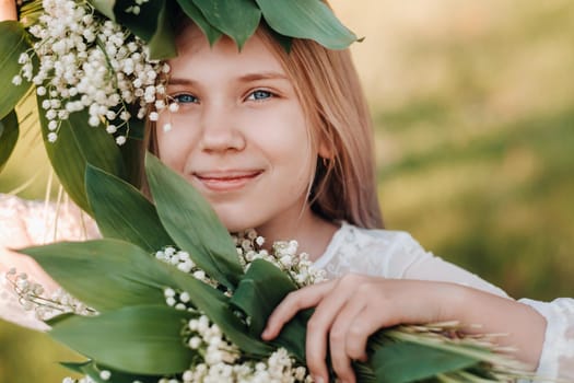 A beautiful nine-year-old blonde girl with long hair in a long white dress, holding a bouquet of lilies of the valley flowers, walking in nature in the Park.Summer, sunset