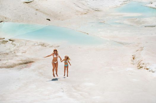 a little girl with her mother in bathing suits and sunglasses on a White mountain, a Family on a Sunny summer day on another planet, Pamukkale, Turkey.