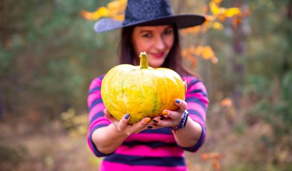 beautiful witch holds out a pumpkin to the camera in the autumn forest