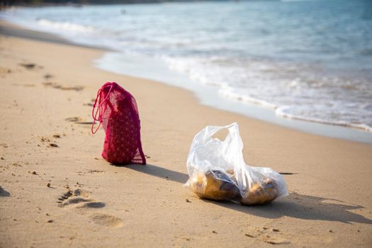 Mesh shopping bag and plastic bag lie on the sandy beach of the sea on a sunny day. ecology of oceans concept